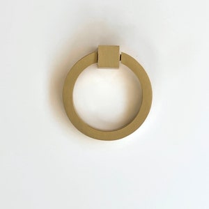 May include: A gold ring pull cabinet handle with a square top.