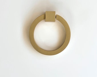 May include: A gold ring pull cabinet hardware with a square top.