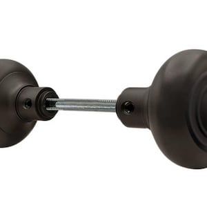 May include: A pair of black door knobs with a round, slightly domed shape. The knobs have a concentric circle design and are connected by a metal rod.