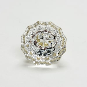 Pode incluir: Um botão de vidro transparente com um design facetado. O botão tem um padrão em forma de estrela no centro.