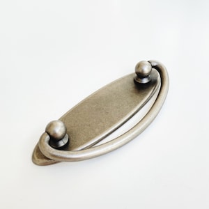 May include: A silver-toned oval-shaped cabinet pull with a curved handle. The handle has a rounded end on each side.