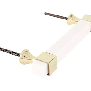 Op de afbeelding: Witte rechthoekige kastgreep met gouden metalen eindkappen en schroeven.