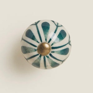 May include: A white ceramic knob with a green and white floral design and a gold center.