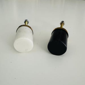 May include: Two cabinet knobs, one white marble and one black, with a gold metal top and a silver screw.
