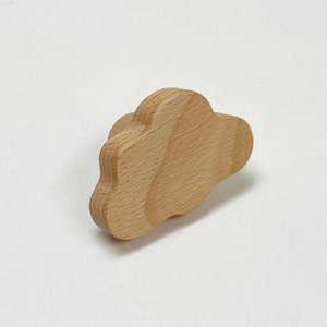 May include: A wooden cloud-shaped ornament in a light brown colour. The cloud has a smooth, rounded surface and is made of natural wood.