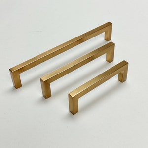 Puede incluir: Tres tiradores de armario de diferentes tamaños en color dorado. Los tiradores son rectangulares con bordes redondeados y un diseño simple y moderno.