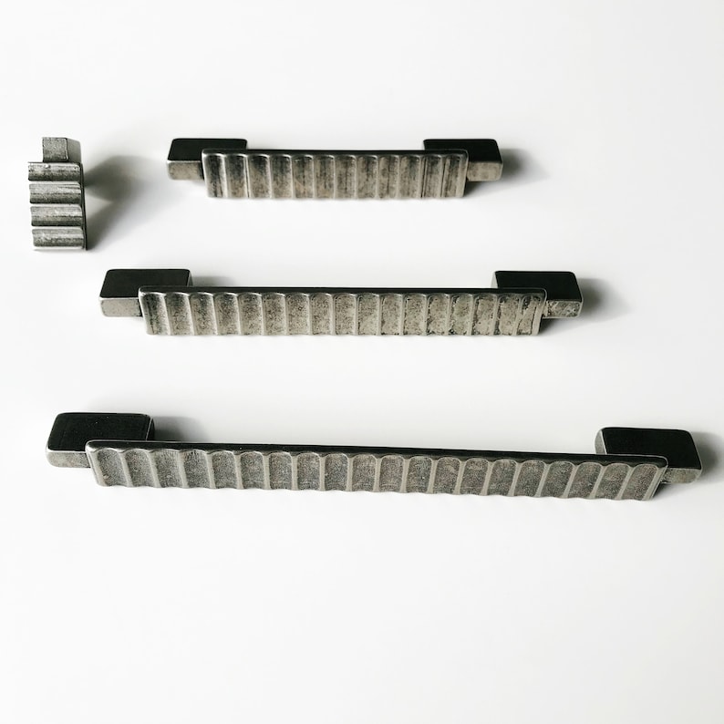 May include: Three silver metal cabinet pulls with a textured, ribbed design. The pulls are different sizes.