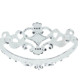 May include: White metal drawer pull with a decorative, ornate design. The pull has a curved shape and a center diamond.
