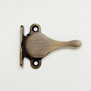 May include: Antique brass window latch with a lever handle. The latch is designed to be mounted on a window frame and has a simple, functional design.