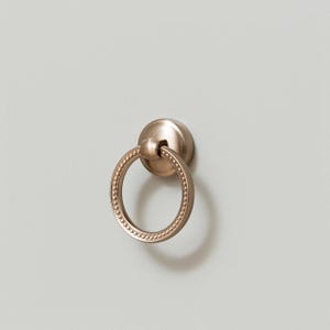 May include: A gold ring pull drawer handle with a beaded edge.