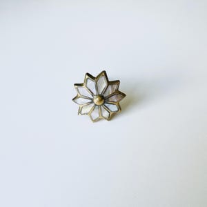 Puede incluir: Un pomo de armario dorado con un diseño de estrella. El centro del pomo está hecho de nácar blanco.