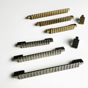 May include: A set of six cabinet pulls in two finishes: brushed brass and aged nickel. The pulls have a ribbed design and are available in two sizes.