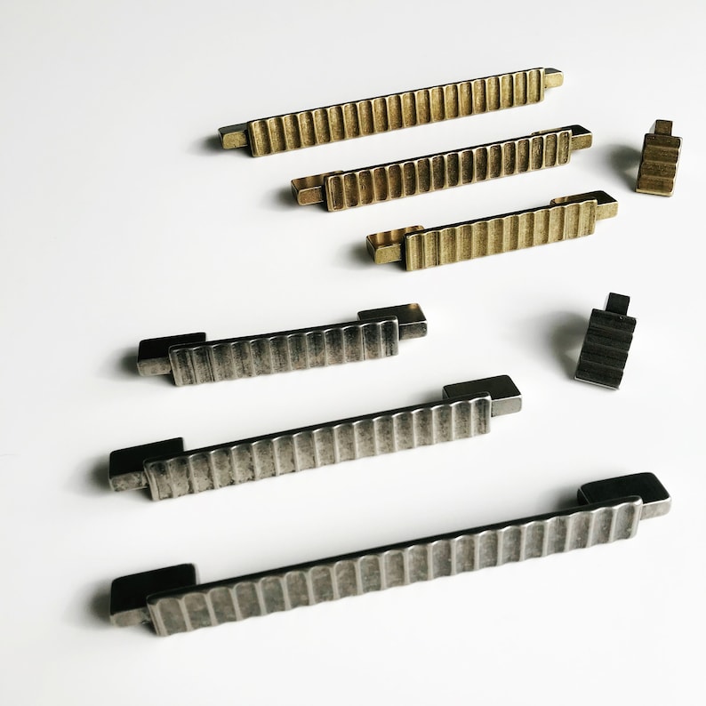 May include: A set of six cabinet pulls in two finishes: brushed brass and aged nickel. The pulls have a ribbed design and are available in two sizes.