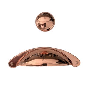 May include: A set of two rose gold cabinet pulls. The larger pull is a curved, half-circle shape. The smaller pull is a round knob.