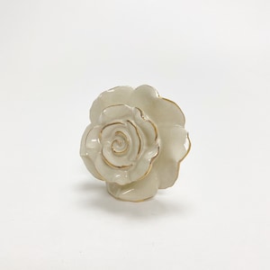 May include: A white ceramic rose door knob with gold accents. The rose is detailed with a swirl pattern in the center.