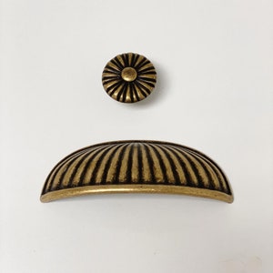 May include: A gold-toned cabinet knob with a fluted design. The knob is round with a raised center and a decorative floral pattern.