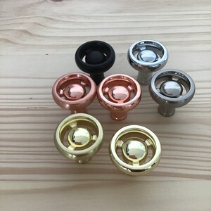 May include: Seven different cabinet knobs with a circular design. The knobs are made of metal and come in a variety of finishes, including black, silver, gold, copper, and brass.