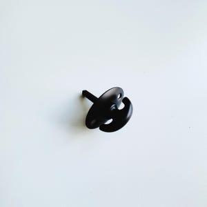 May include: Black metal hook with a rounded base and a single hook. The hook is attached to a flat, round base with a screw.
