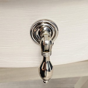 May include: A polished nickel cabinet knob with a round base and a teardrop-shaped handle.