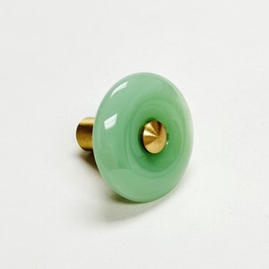 May include: A green glass cabinet knob with a brass base. The knob has a raised, circular design in the center.