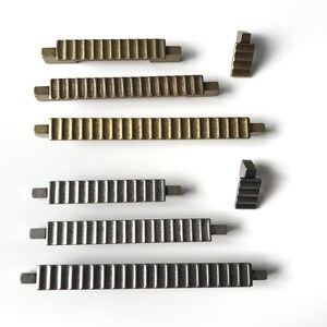 May include: Five cabinet pulls in two different finishes. Two pulls are gold with a ribbed design, two are silver with a ribbed design, and one is a small corner pull in silver.