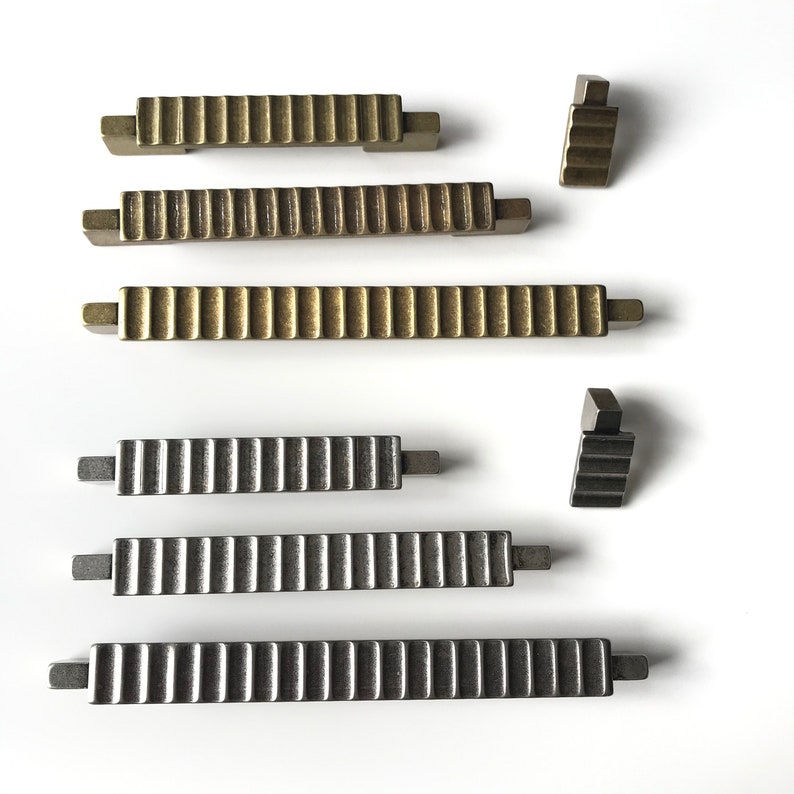May include: Five cabinet pulls in two different finishes. Two pulls are gold with a ribbed design, two are silver with a ribbed design, and one is a small corner pull in silver.
