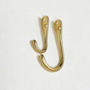 May include: Two gold-toned metal hooks with a curved design. The hooks have two holes at the top for mounting.