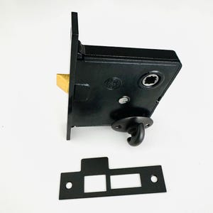 May include: Black door latch with a brass latch and a hook. The latch is attached to a black metal plate with two holes.