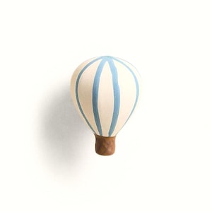 May include: A wall hook shaped like a hot air balloon with a cream-colored balloon canopy featuring vertical light blue stripes. The basket section of the balloon is made of a textured brown material, providing a contrast to the upper portion.