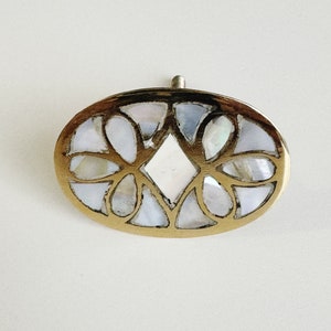 May include: Oval-shaped brass cabinet knob with a decorative design featuring a diamond-shaped center and surrounding floral motifs. The center and floral motifs are made of iridescent mother-of-pearl.
