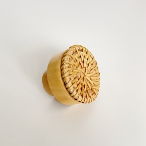 May include: A round wooden knob with a woven rattan top. The knob is light brown in color.
