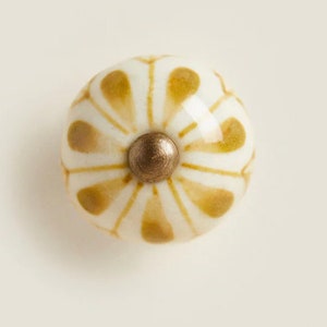 May include: A white ceramic knob with a gold center and a brown floral pattern.