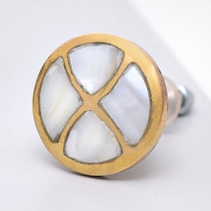 Puede incluir: Un pomo de armario redondo de latón con una incrustación de nácar blanco en un patrón geométrico.