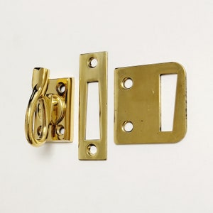 May include: Three brass door hardware pieces: a hook with a loop, a rectangular plate with a slot, and a rectangular plate with a slot and two holes.