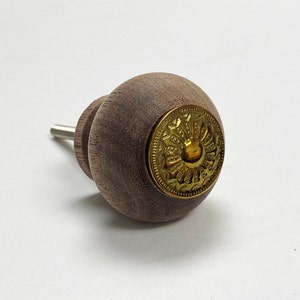 May include: A wooden knob with a gold metal decorative detail. The knob is brown and has a circular shape.