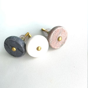 May include: Three round marble cabinet knobs with gold accents. The knobs are in shades of grey, white, and pink.