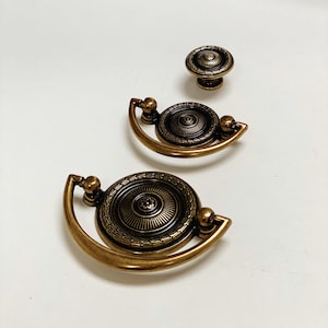 May include: Three antique brass cabinet knobs with ornate designs. The knobs are in different sizes and feature a circular shape with a raised center.