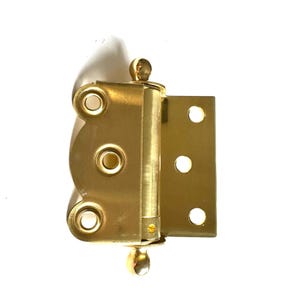 Puede incluir: Una bisagra de puerta decorativa de color dorado con un borde redondeado y festoneado y dos pomos decorativos.