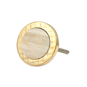 Könnte beinhalten: Ein runder, goldfarbener Schrankknopf mit einer weißen, strukturierten Mitte. Der Knopf hat eine strukturierte, gehämmerte Goldoberfläche.