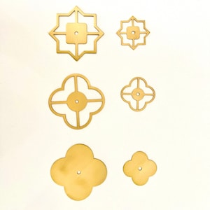 May include: Six gold metal decorative accents in various geometric shapes. The accents have a hole in the centre and are designed to be used as drawer pulls or cabinet knobs.