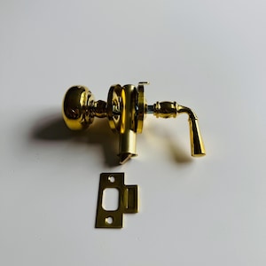 Puede incluir: Un juego de pomo y palanca para puerta de color dorado con un pomo redondo y una palanca con una manija curva. El juego incluye una placa de golpe.