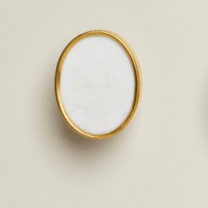 May include: A white round knob with a gold metal rim. The knob is smooth and has a slightly raised edge.