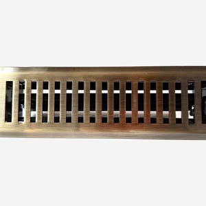 May include: A rectangular floor register vent cover with a brushed antique brass finish. The metal cover features a series of vertical slats and a small black adjustment lever on the right side to control airflow through the internal black dampers.