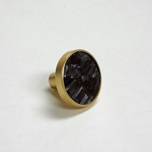 May include: A gold round cabinet knob with a black patterned inlay.