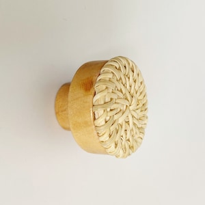 May include: A wooden knob with a woven rattan top. The knob is a light brown color and the rattan is a natural beige color.