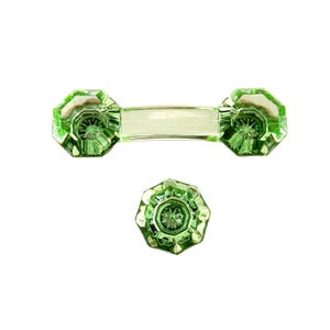 May include: A set of light green glass hardware consisting of one horizontal drawer pull with two faceted, octagonal ends and one matching single octagonal knob. Both pieces feature a starburst pattern at the center of the faceted glass surface.