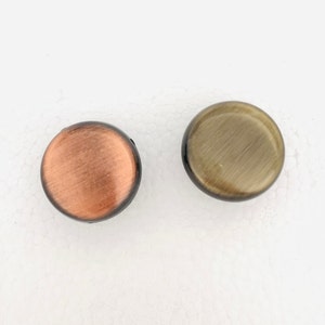 May include: Two round, decorative knobs with a brushed metal finish. One knob is copper colored and the other is gold colored.