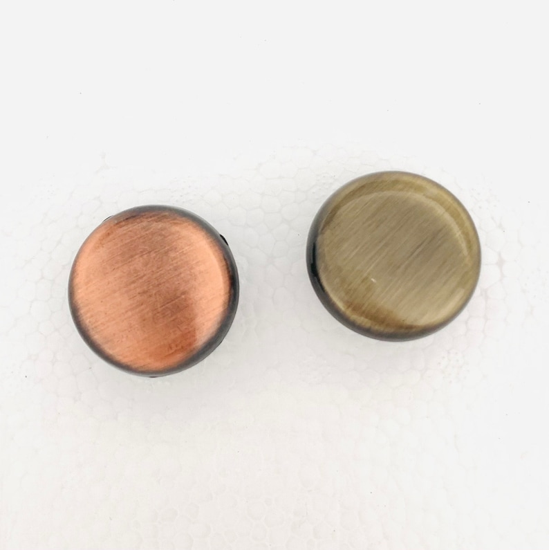 May include: Two round, decorative knobs with a brushed metal finish. One knob is copper colored and the other is gold colored.