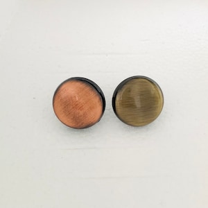 May include: Two round, flat earrings with a brushed metal finish. One earring is copper colored and the other is a dark green.