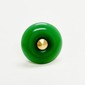 May include: A green glass cabinet knob with a gold center. The knob has a circular shape and a slightly raised design.